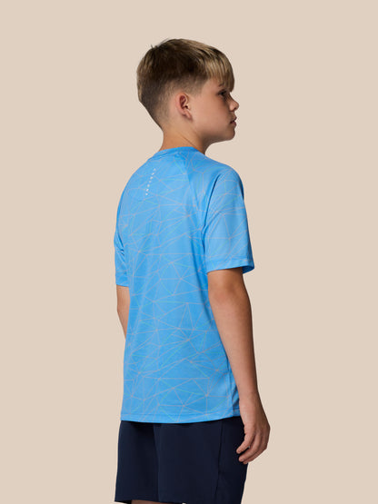 Back view of a boy in a blue geometric print short sleeve T shirt with Castore logo running down the back