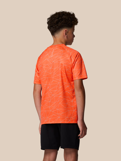 Back view of a young wearer in bright orange all over geometric print short sleeve T shirt with Castore logo on the back neck.