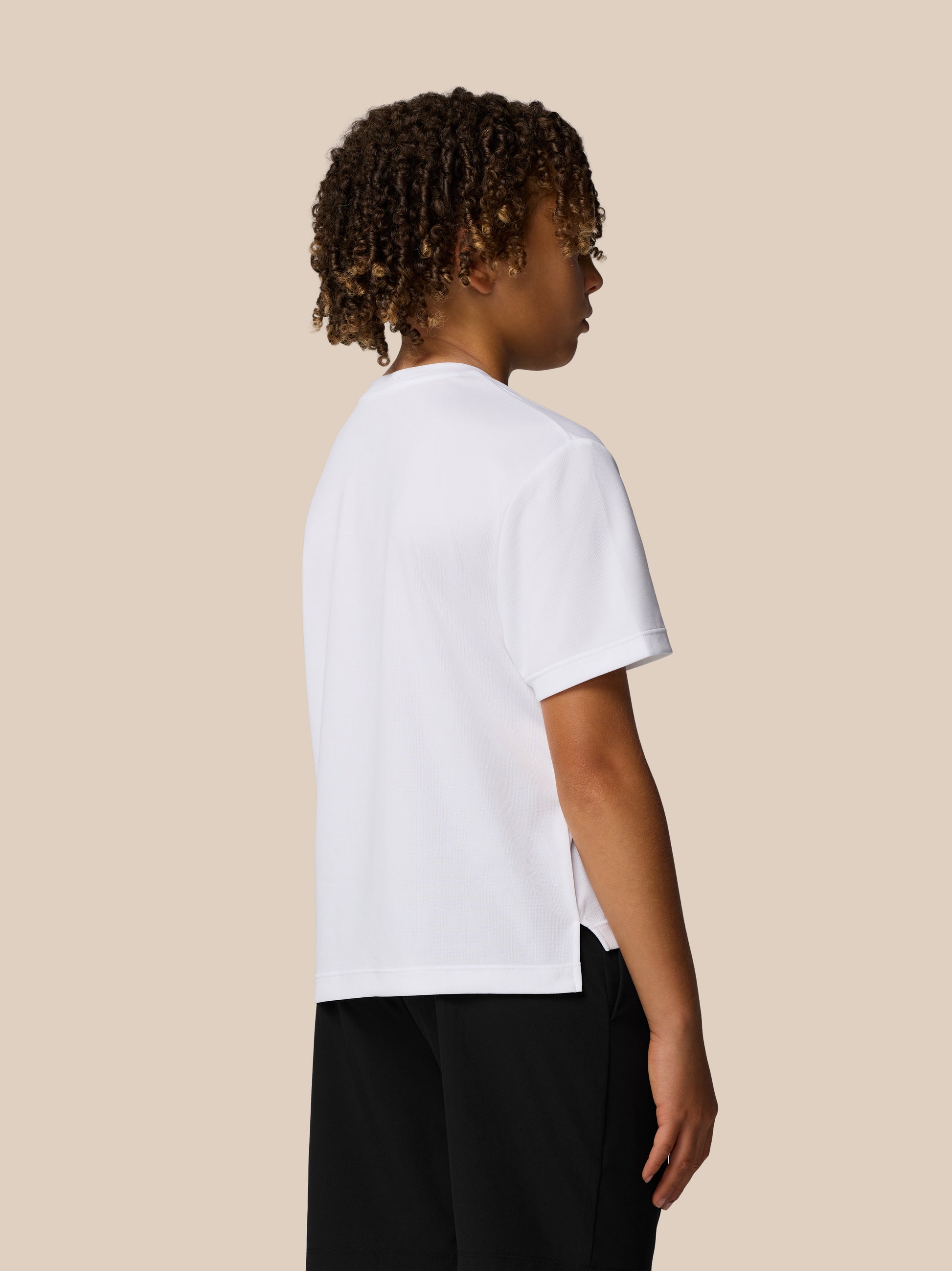 Side profile of a young boy wearing a white Junior’s Adapt Short Sleeve T Shirt against a beige background