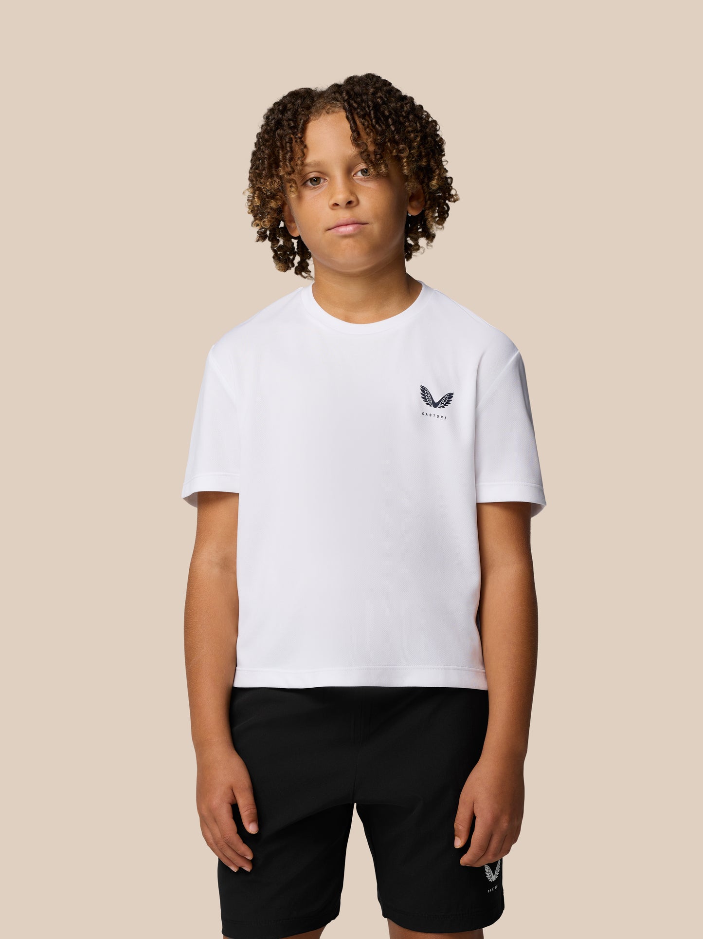 Young model wearing a white Junior Adapt Short Sleeve T Shirt with reflective Castore logo on the chest