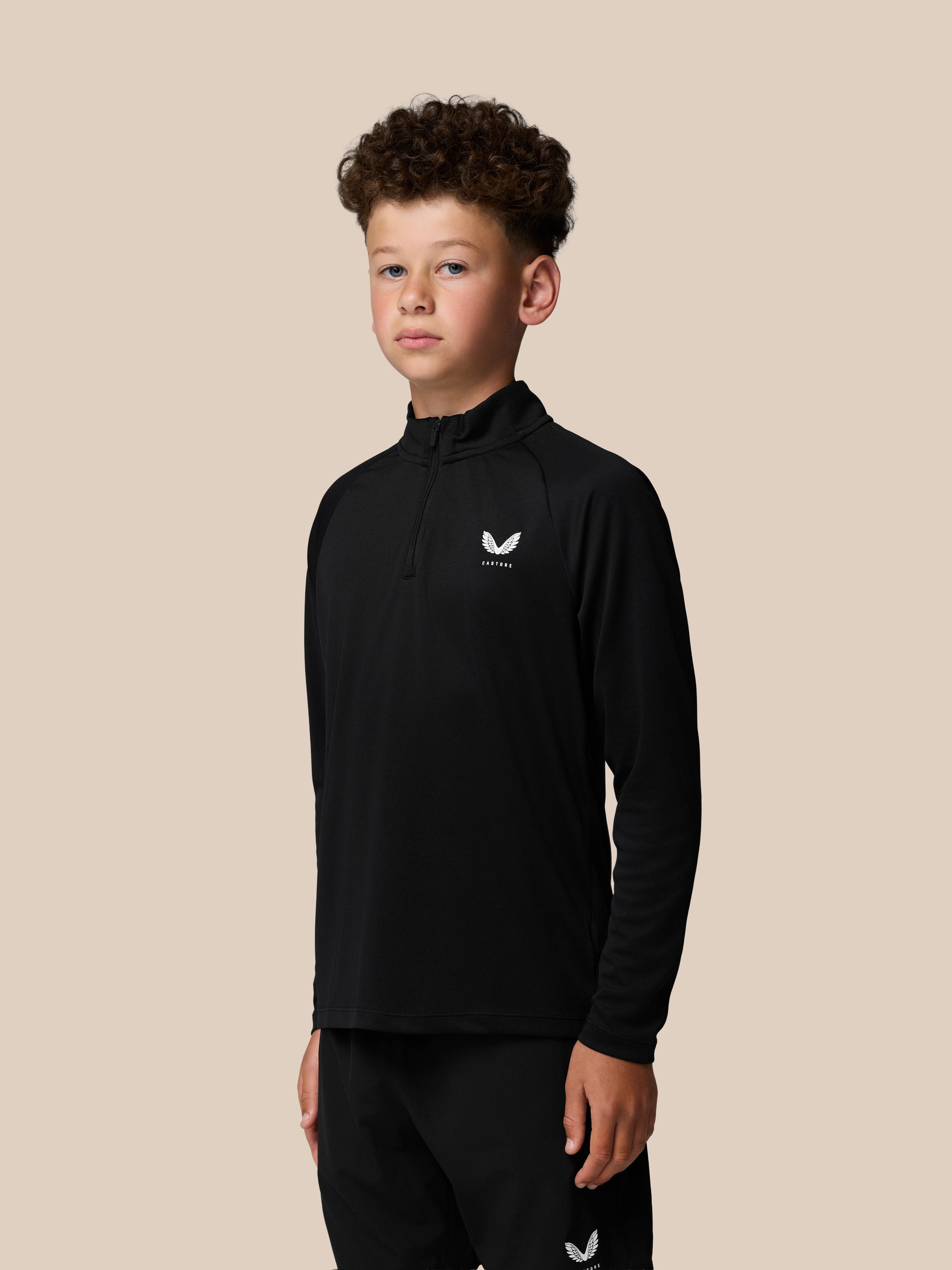 Front view of a boy wearing a black Junior Adapt Lightweight Quarter Zip with a white Castore logo on the left chest.