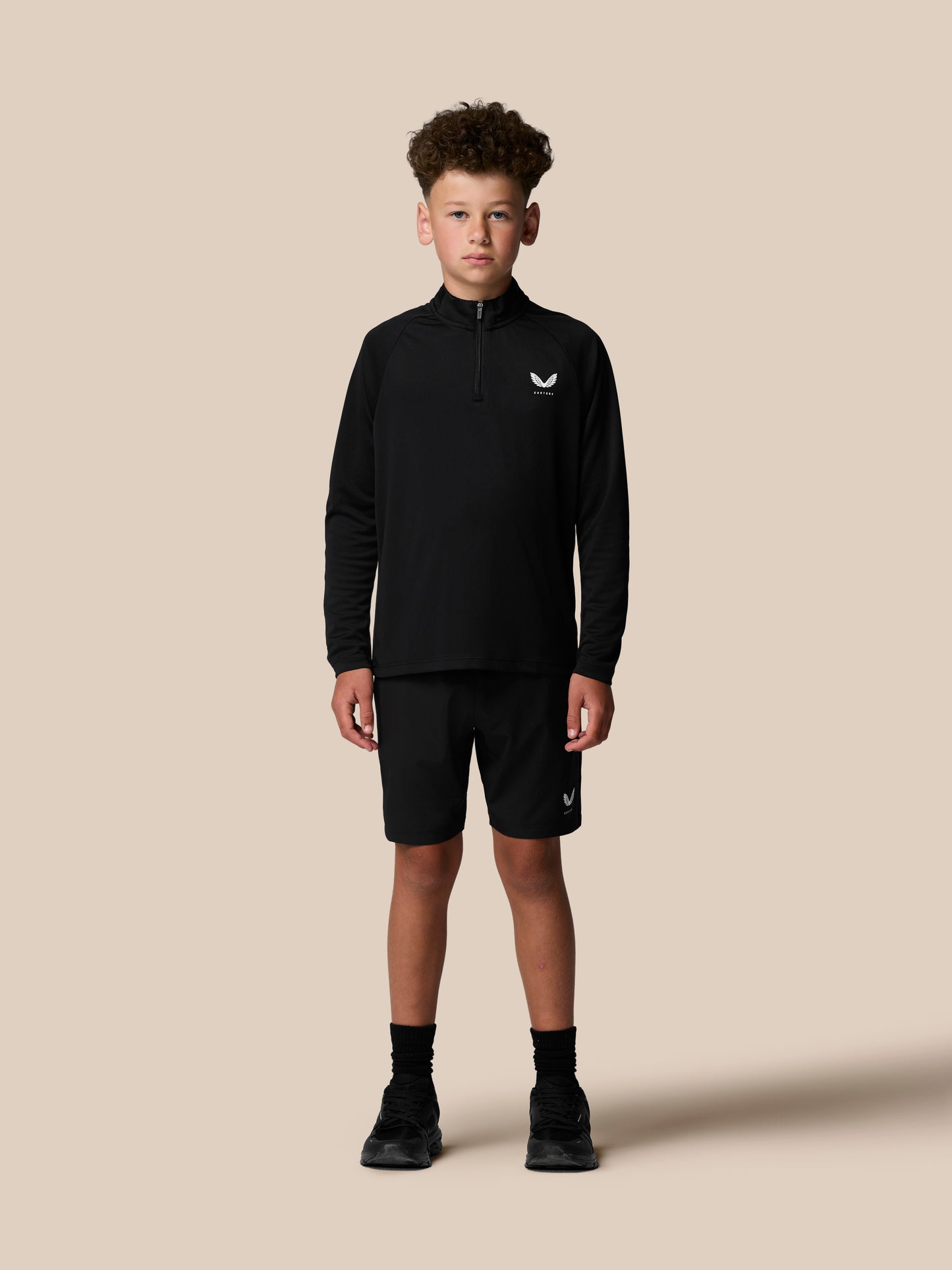 Back view of a boy in a black quarter zip showing vertical Castore branding along the upper back.