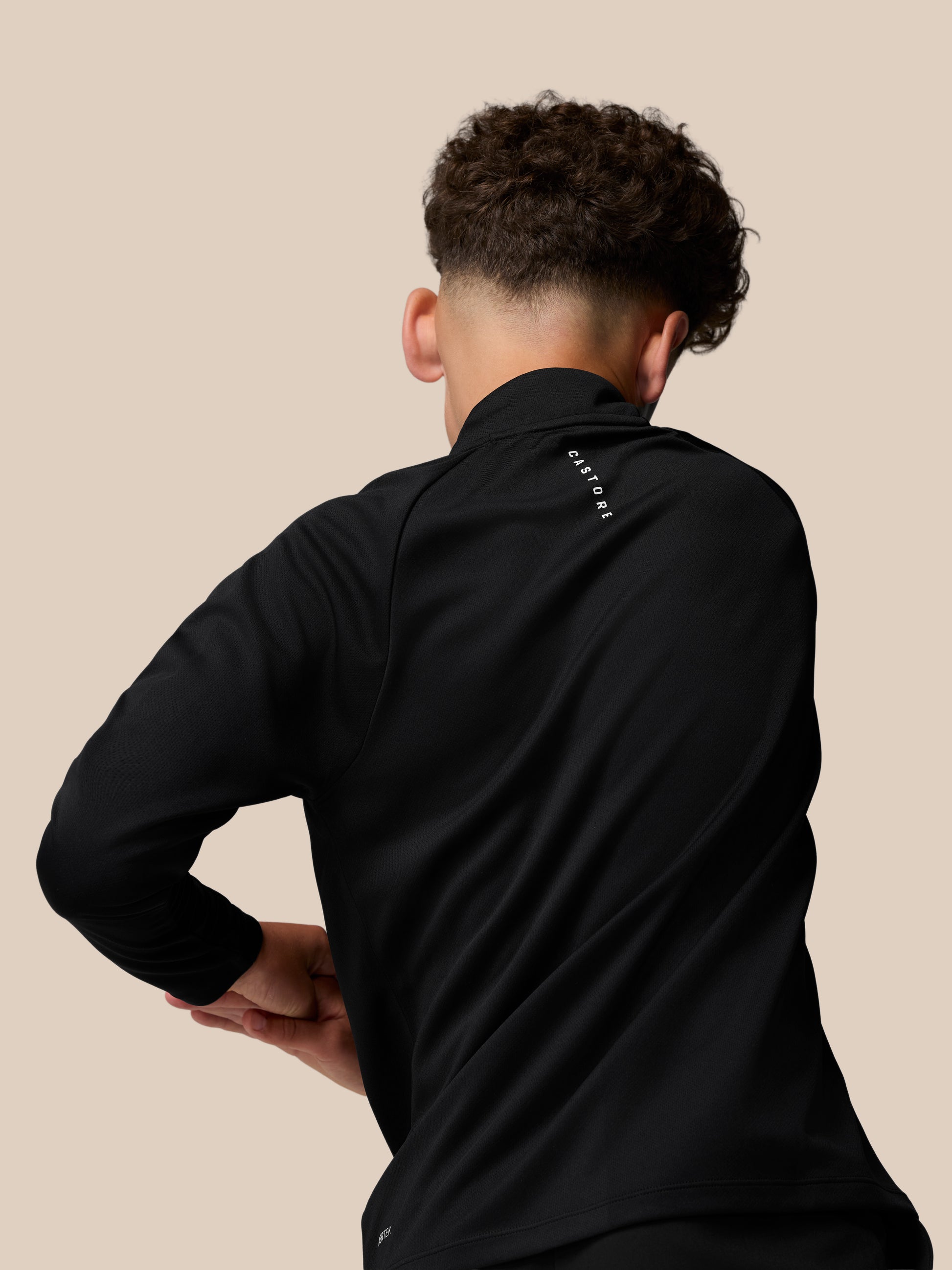 Back view of a young person in a black Castore Adapt lightweight quarter zip, with Castore logo along the back neck.