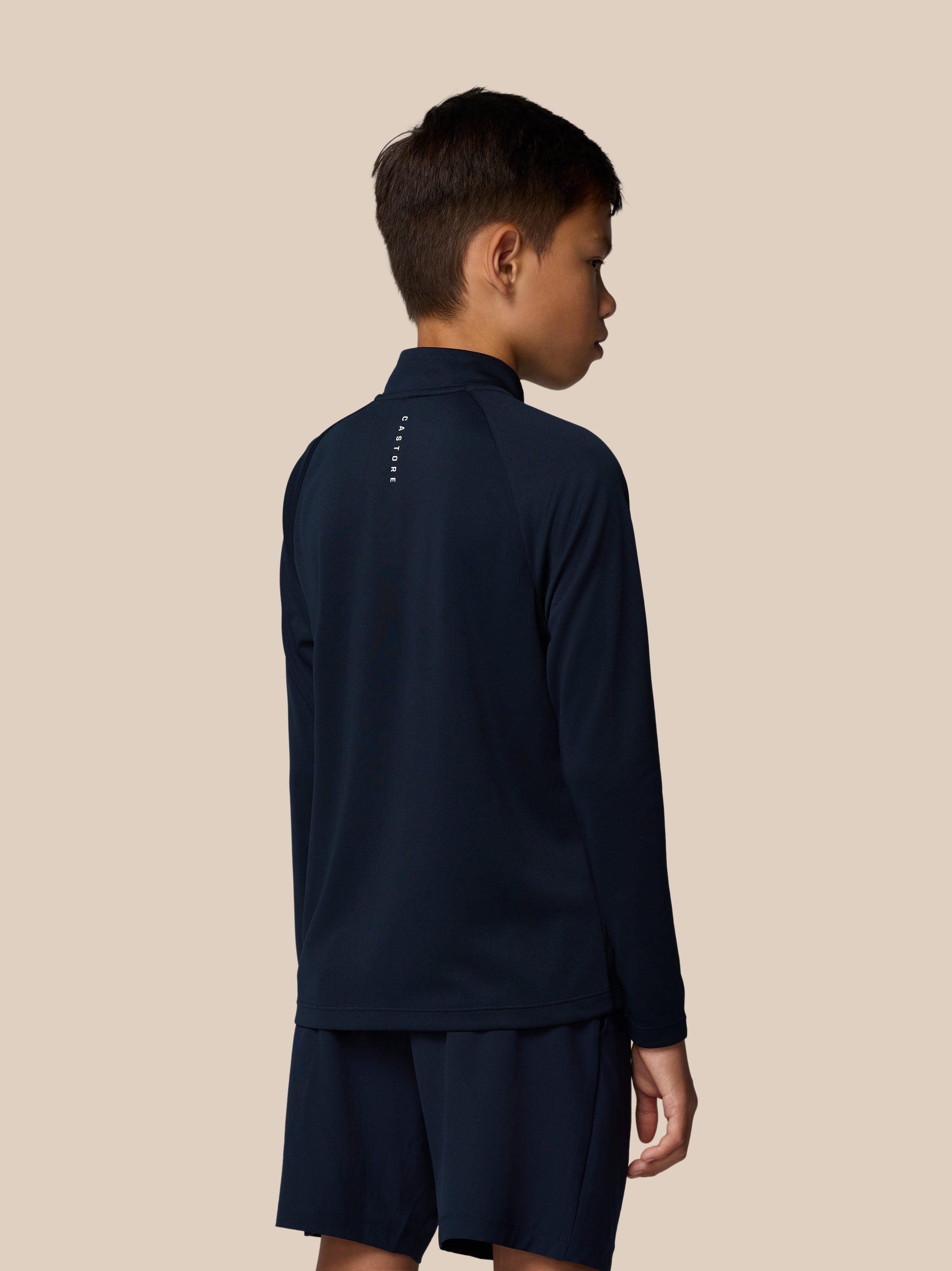 Back view of a young boy in navy Adapt Lightweight Quarter Zip showing vertical branding along the back of the neck