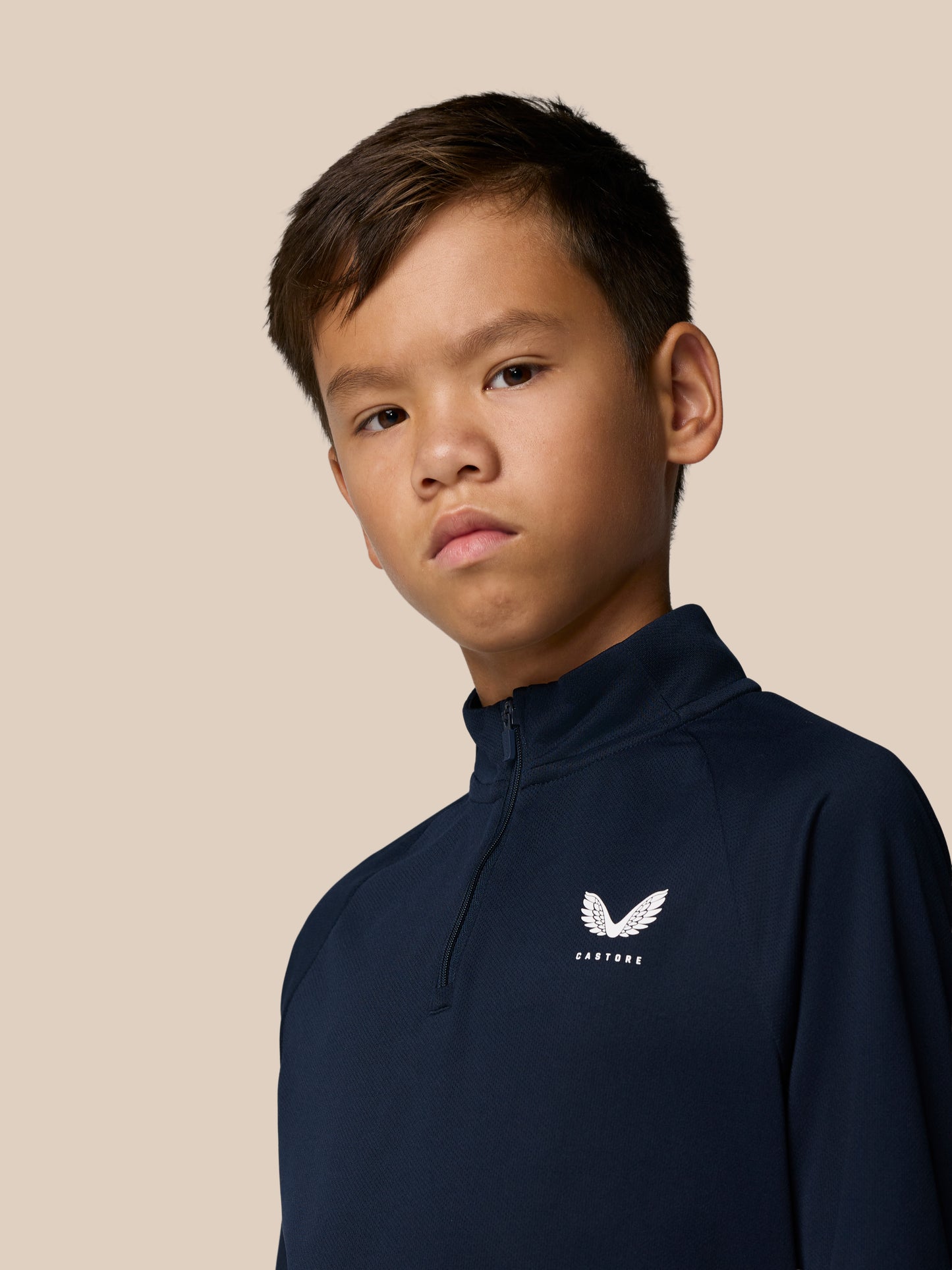 Young boy wearing navy Junior’s Adapt lightweight quarter zip with front zipper and Castore wing logo on the chest.