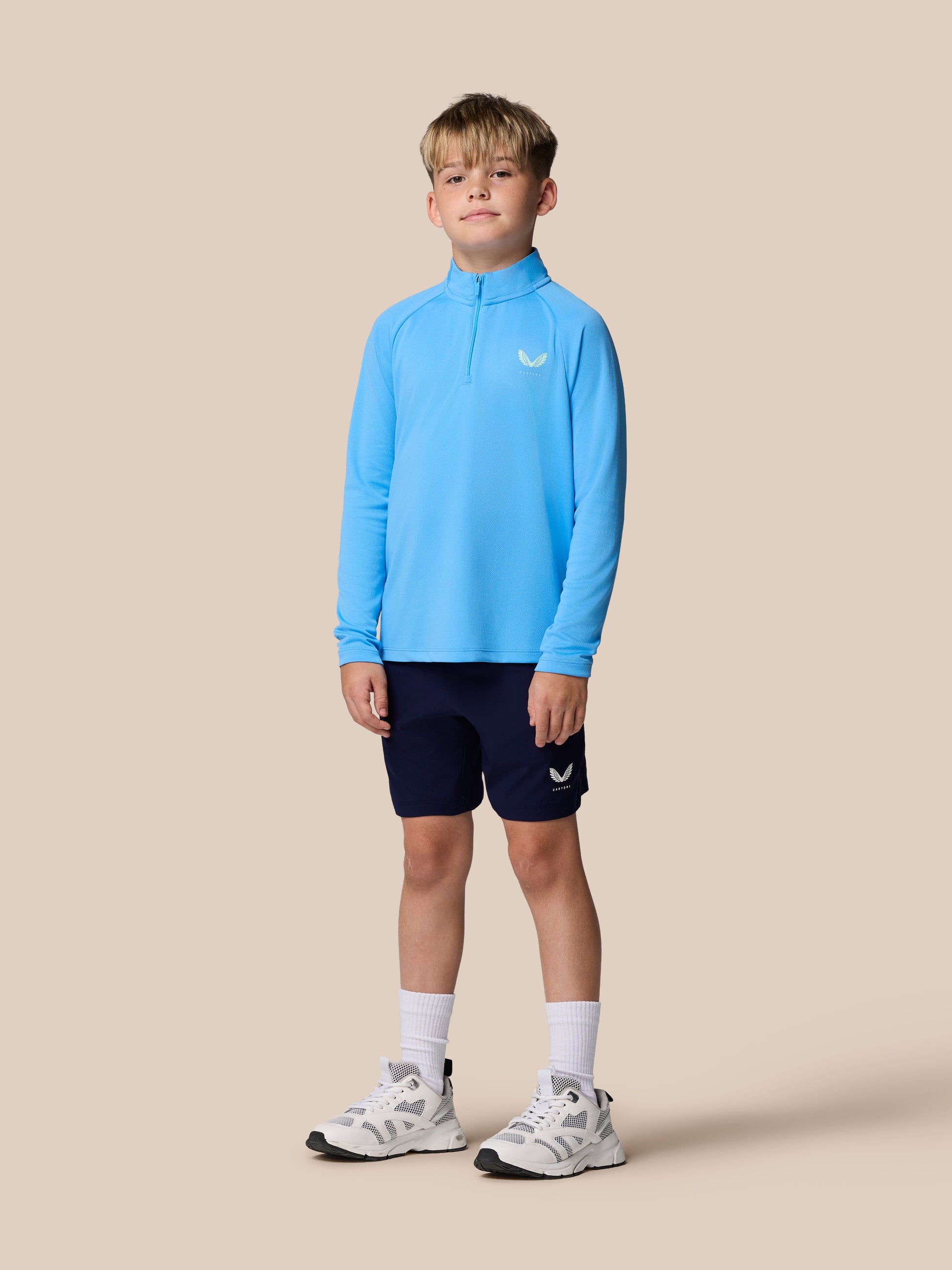 Young boy wearing a light blue junior Adapt Training quarter zip top with a chest logo.