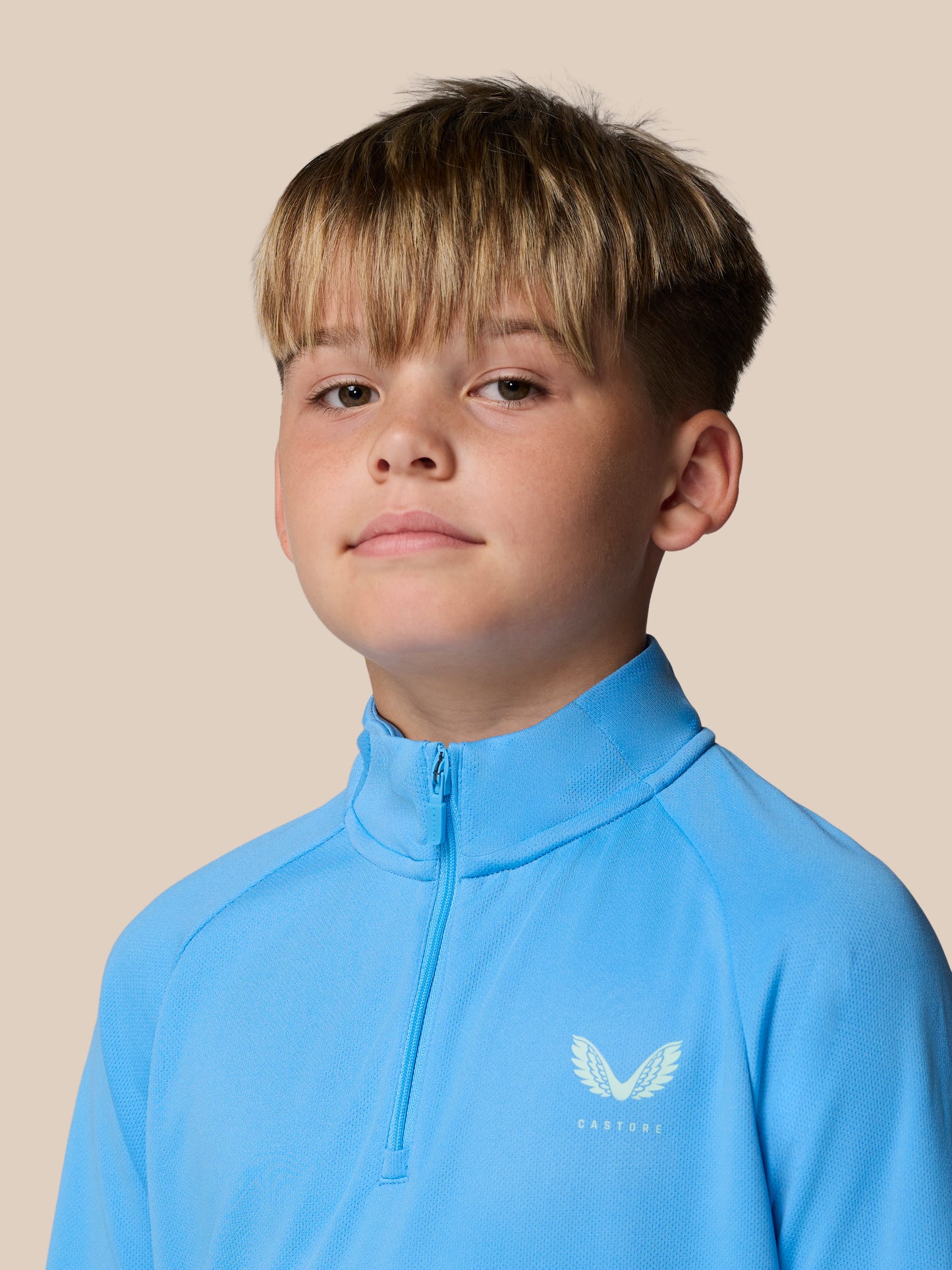 Close-up of a young boy in a light blue quarter zip training top with a winged Castore logo on the chest