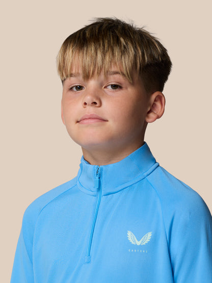 Close-up of a young boy in a light blue quarter zip training top with a winged Castore logo on the chest