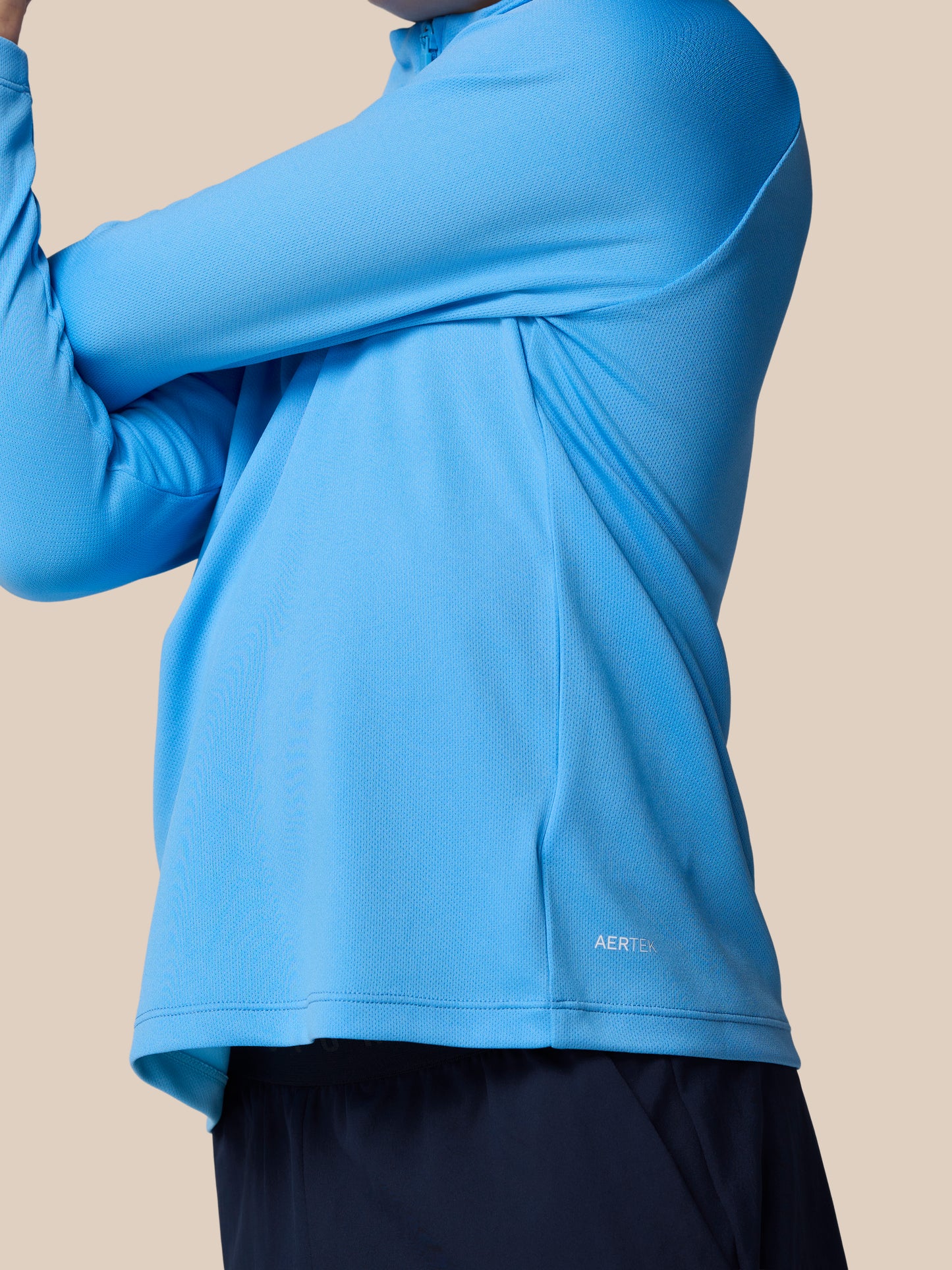 Close-up of a light blue junior Adapt Training quarter-zip top on a model, featuring textured knit fabric and the AerTek logo at the hem.