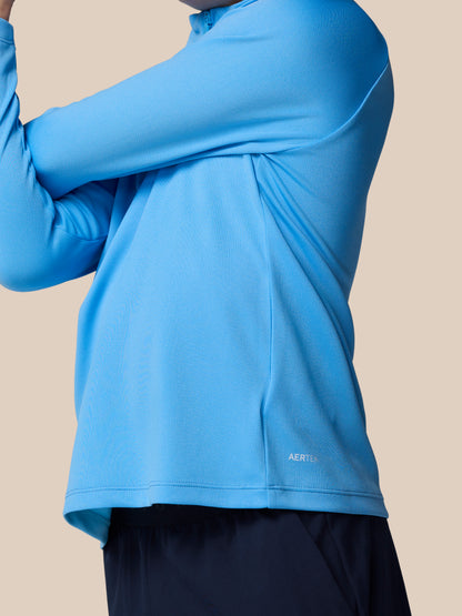 Close-up of a light blue junior Adapt Training quarter-zip top on a model, featuring textured knit fabric and the AerTek logo at the hem.