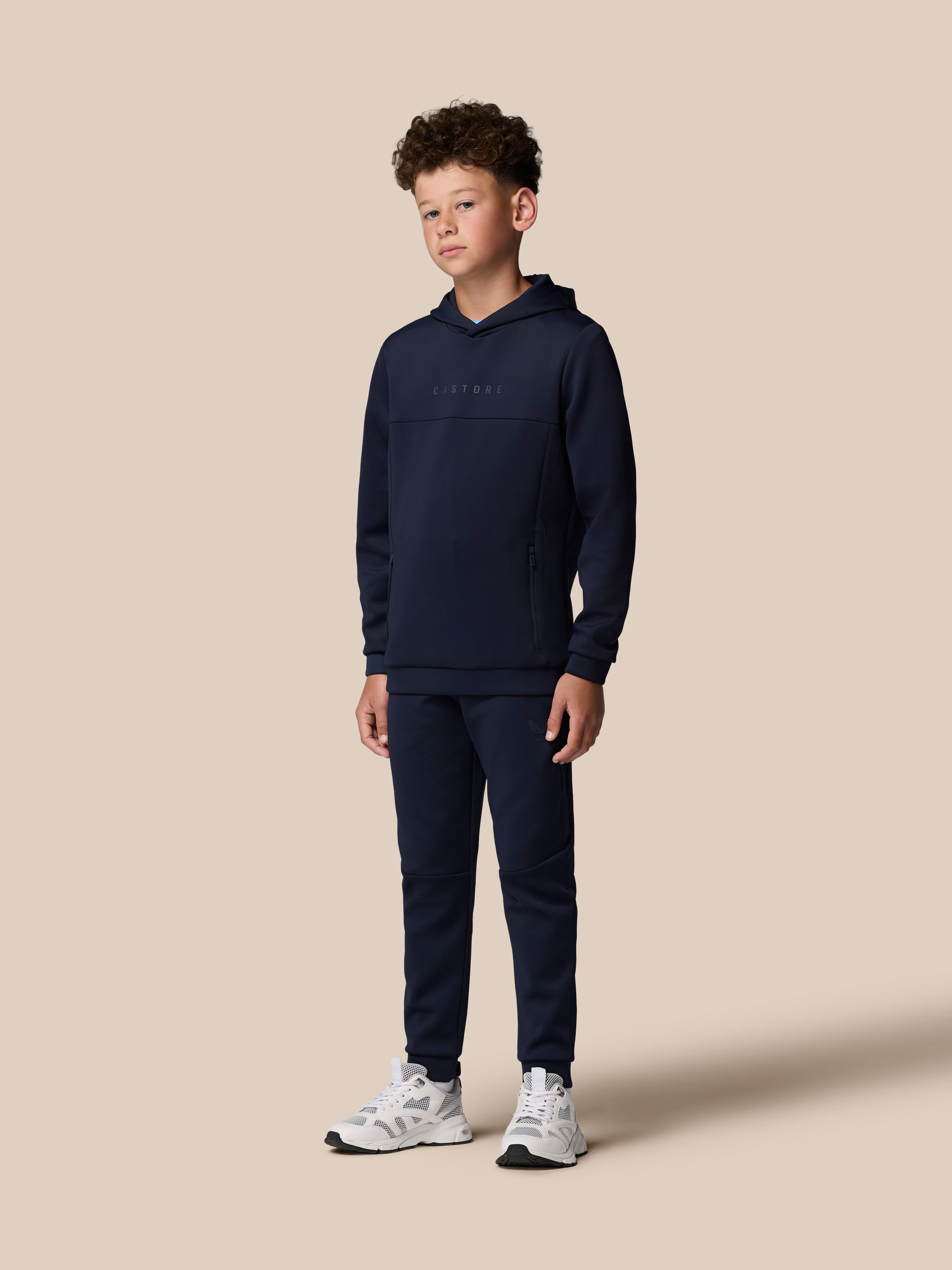 Front view of a young model wearing a navy Junior’s Flex Scuba Long Sleeve Hoodie with Castore wordmark on the chest