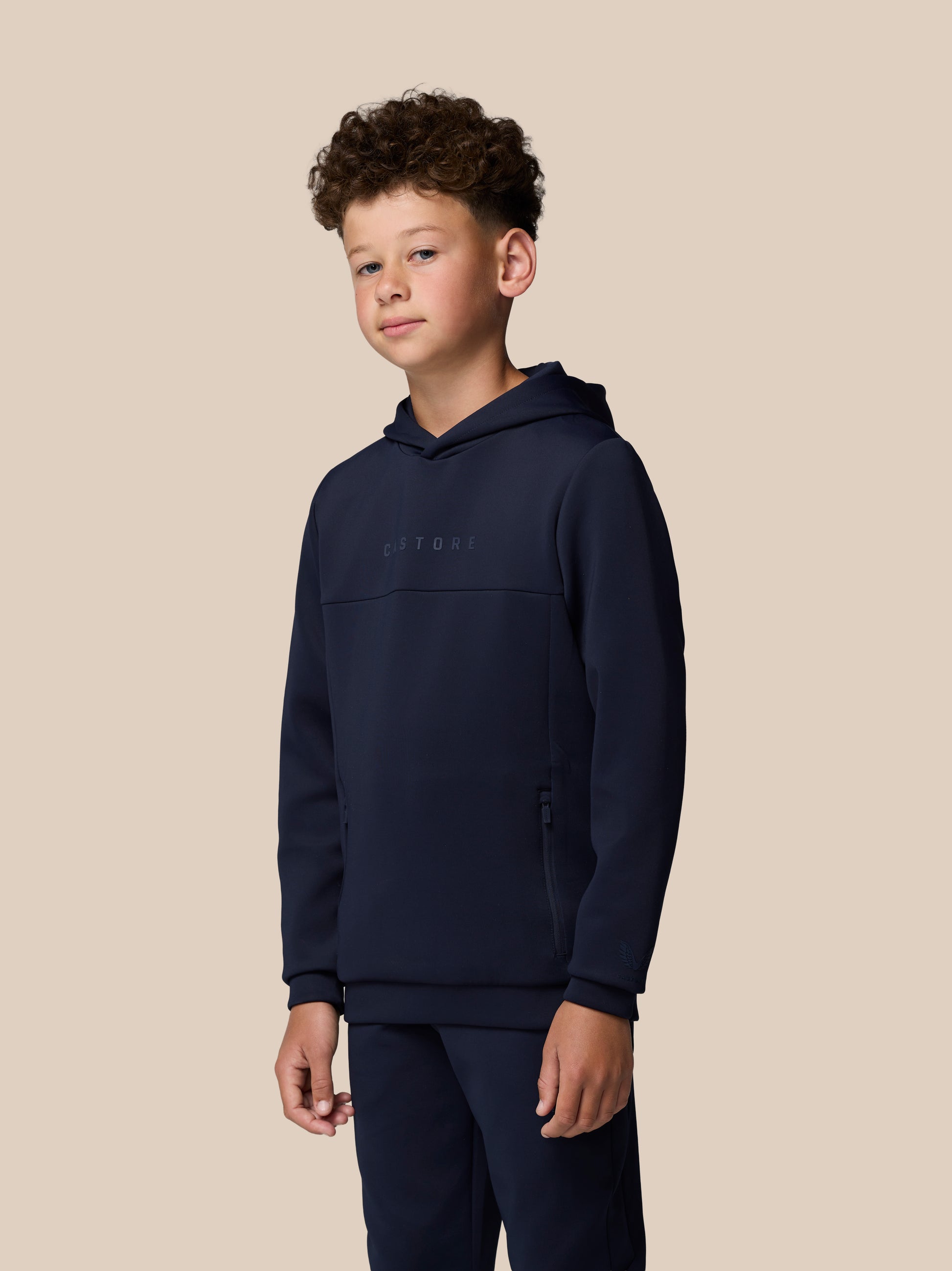Full body shot of a young model in a navy hoodie and matching joggers with hood down and Castore branding on the chest