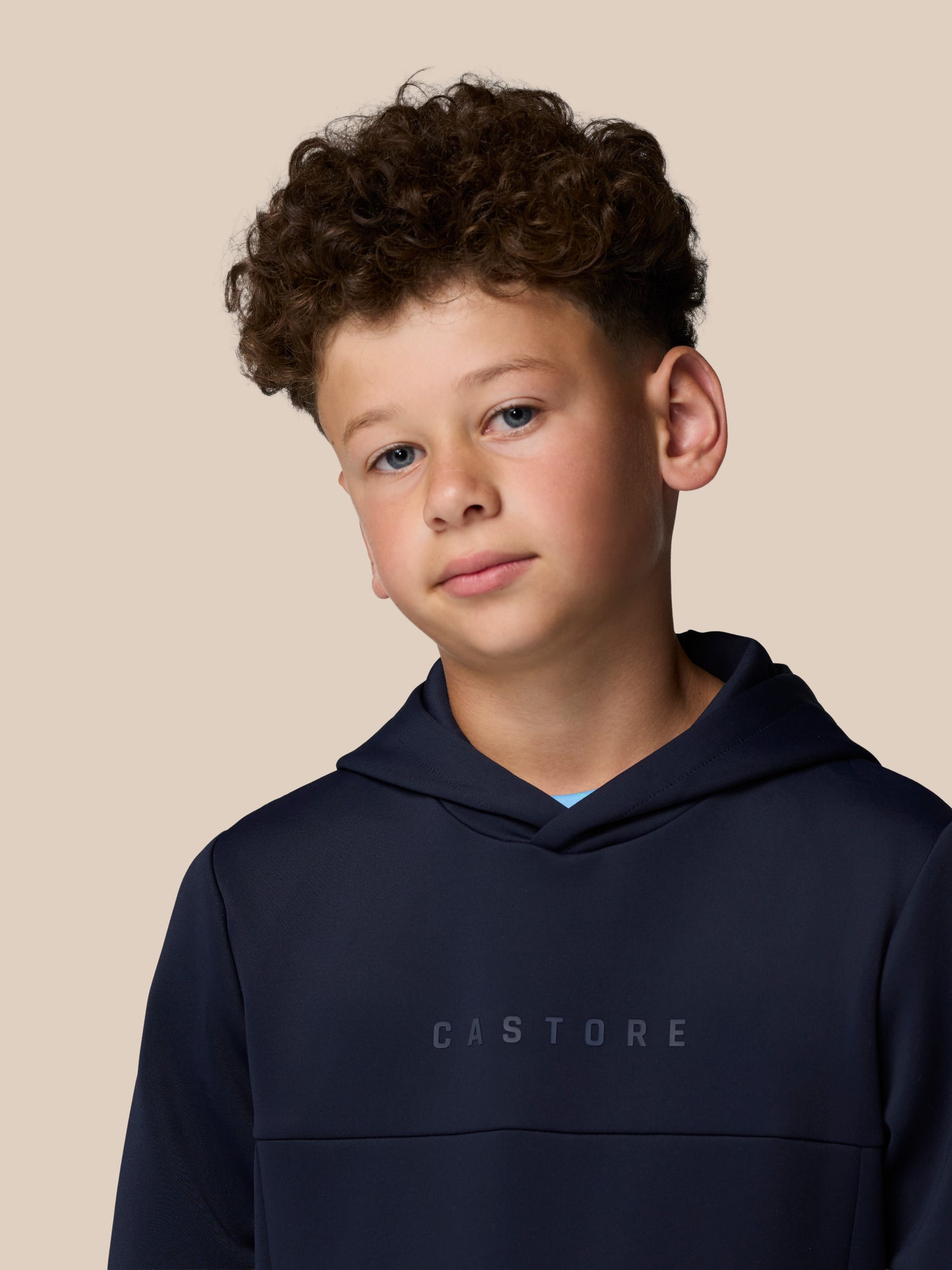Young boy wearing a navy Castore hoodie against a beige studio background