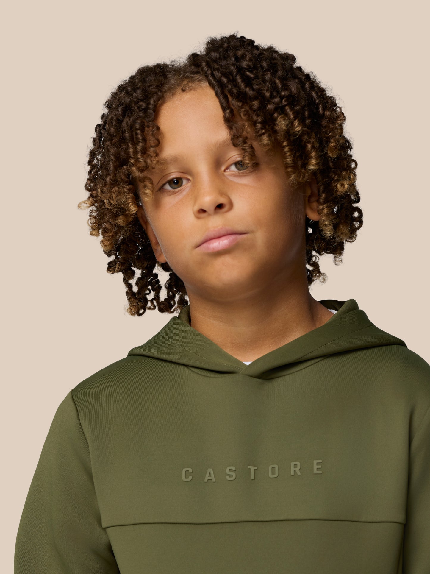 Close up of a young model wearing an olive green hoodie with CASTORE lettering across the chest.