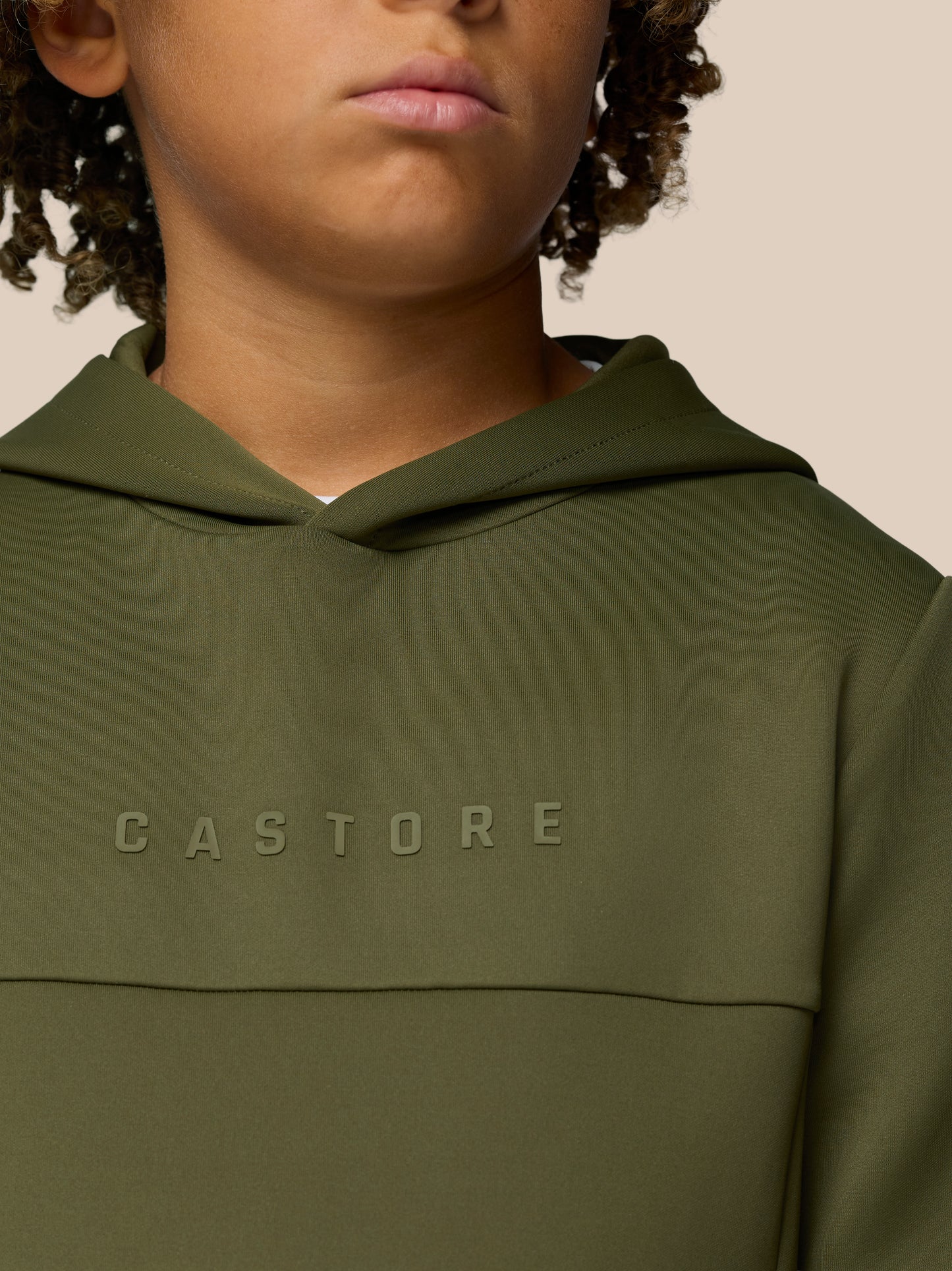 Close up of an olive green Castore hoodie worn by a person, with CASTORE lettering across the chest.