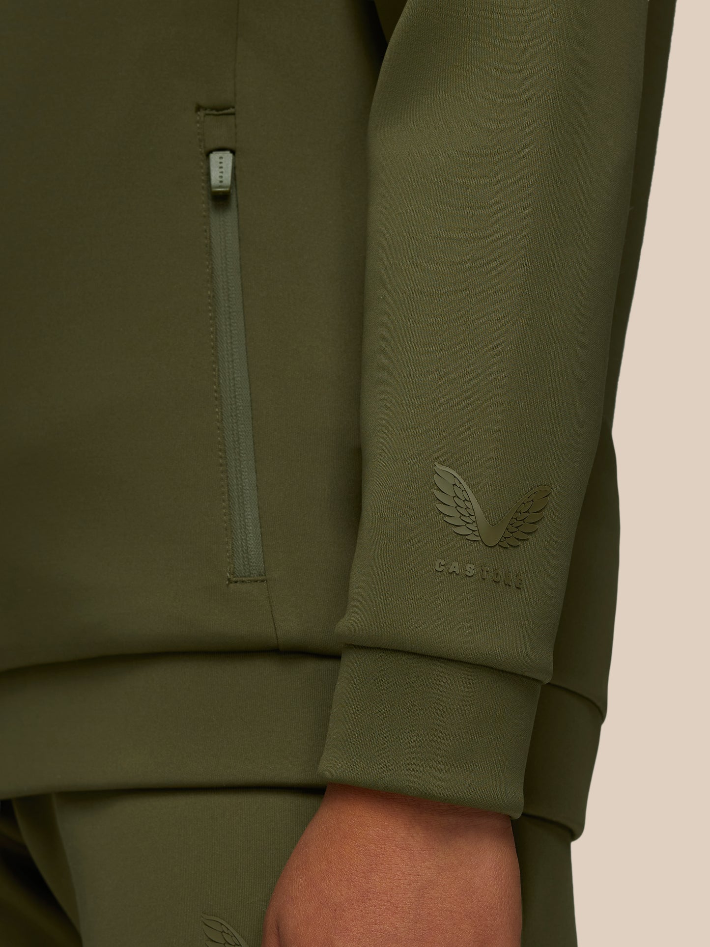 Close-up of olive green Junior’s Flex Scuba hoodie sleeve with a vertical zipper and Castore wing emblem.