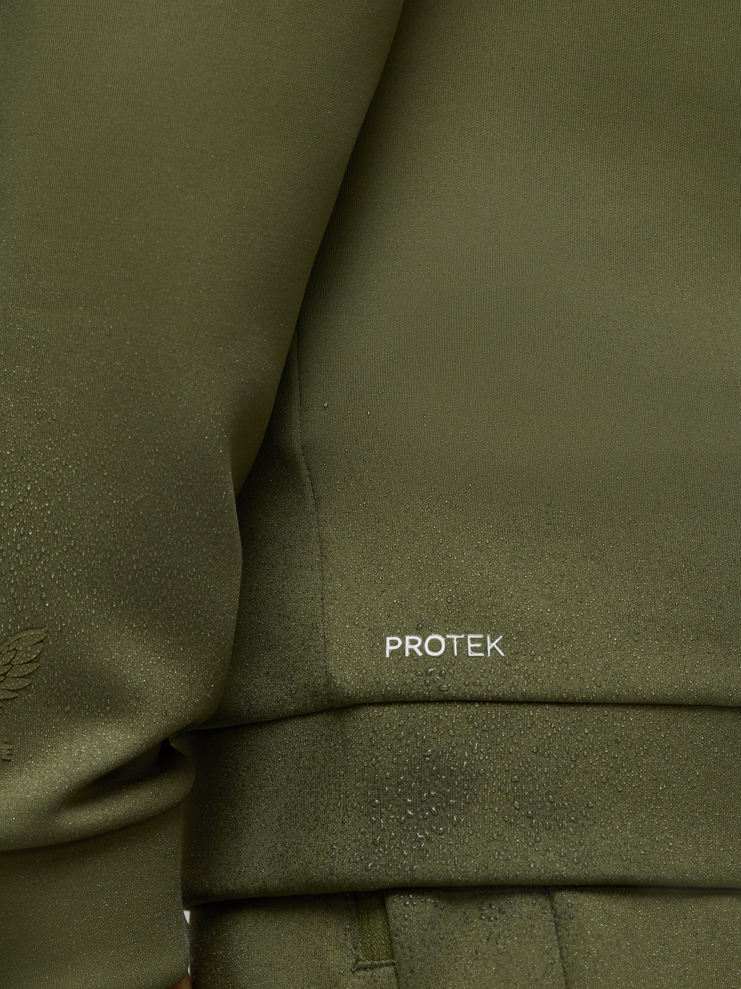 Close-up of olive green scuba fabric with water droplets and PROTEK logo on sleeve