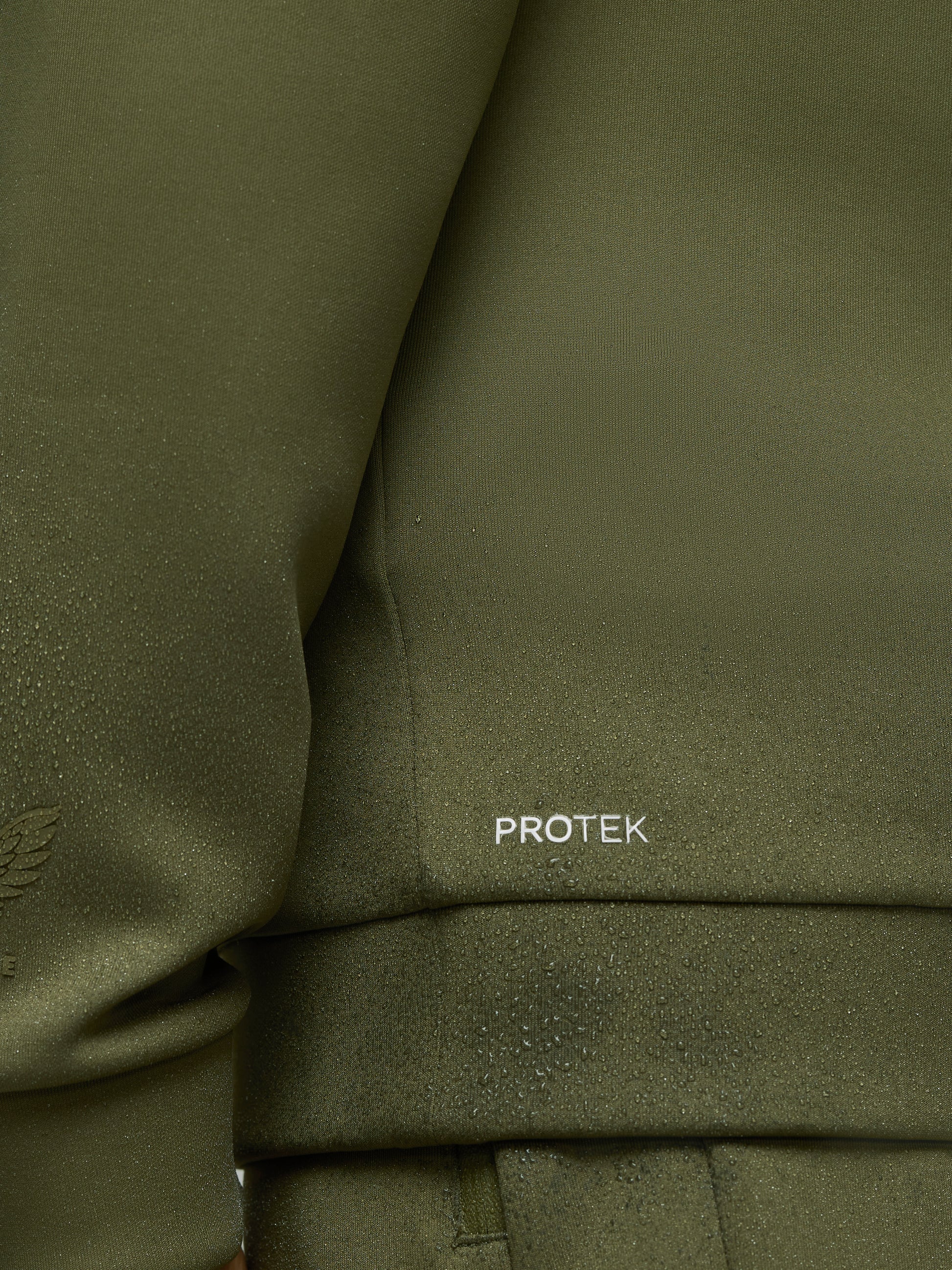 Close-up of olive green scuba fabric with water droplets and PROTEK logo on sleeve
