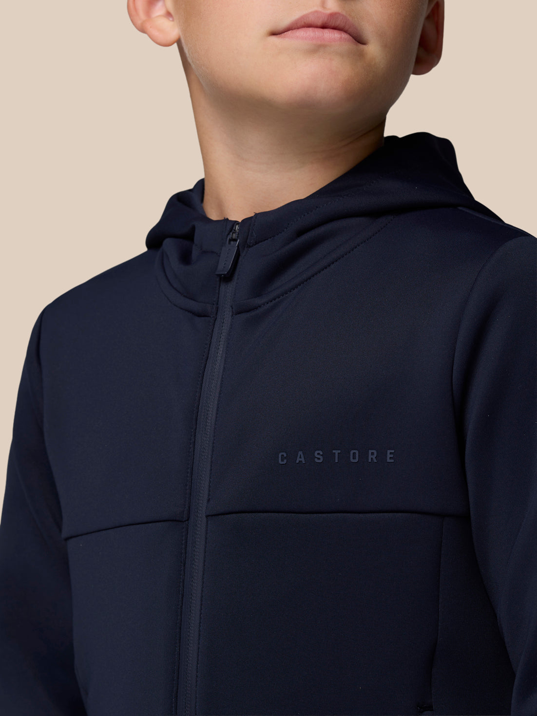 Close-up of a boy in a navy zip through jacket showing Castore wordmark on chest and hood
