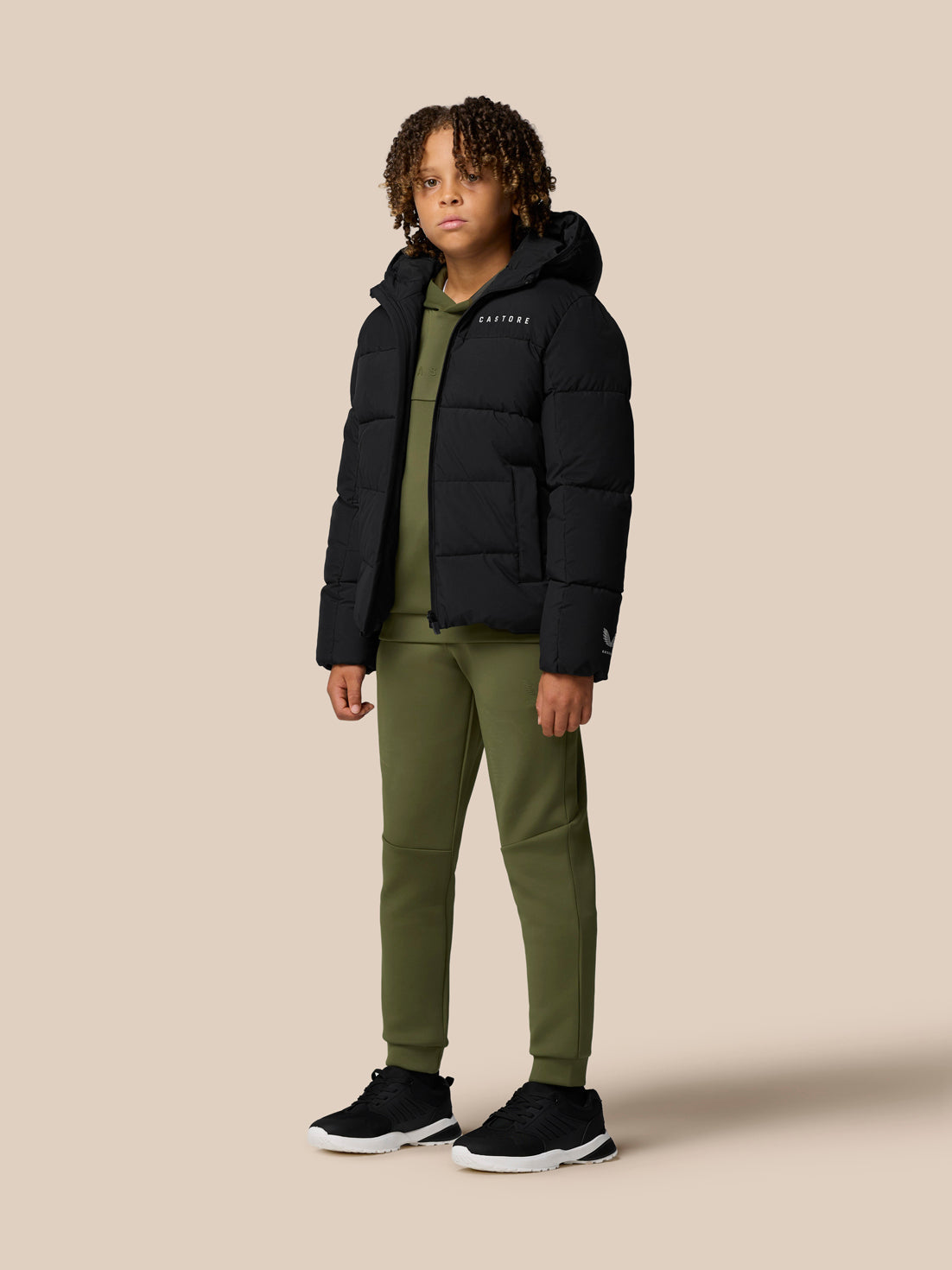 Profile view of child wearing black hooded Quilts puffer jacket with olive green pants