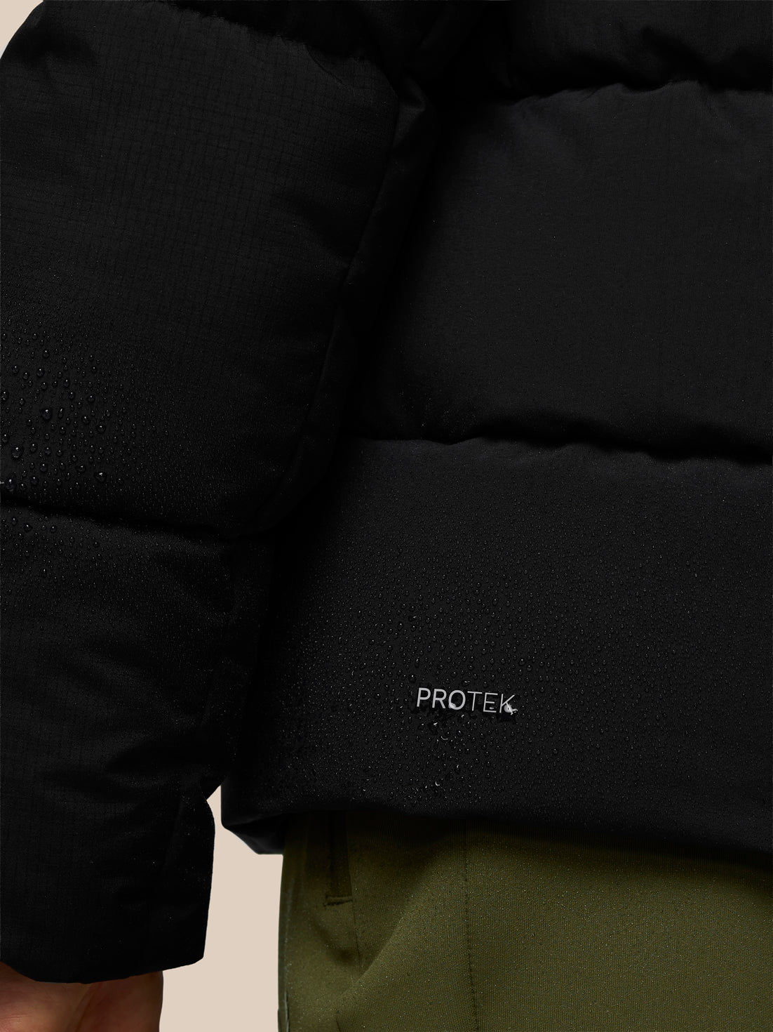 Close up of black Quilts Puffer Jacket fabric with water droplets and ProTek branding