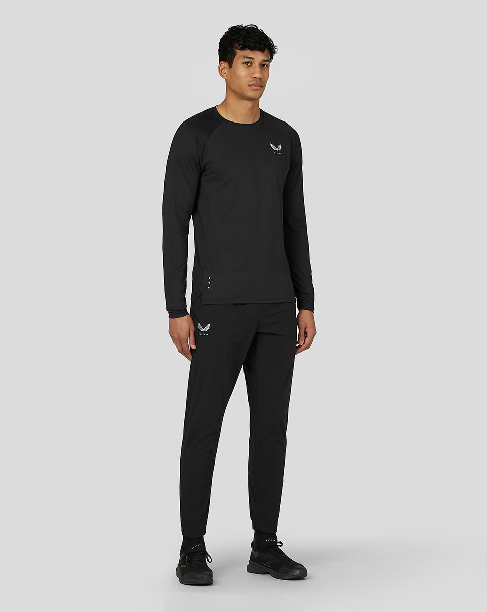 Model in black Castore active wear: long sleeve top with logo on chest and matching joggers with logo on the thigh