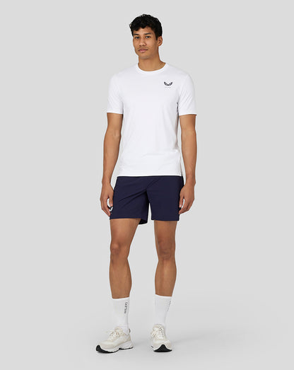 Full body shot of a man wearing a white performance short sleeve T shirt with Castore logo on the chest and navy shorts
