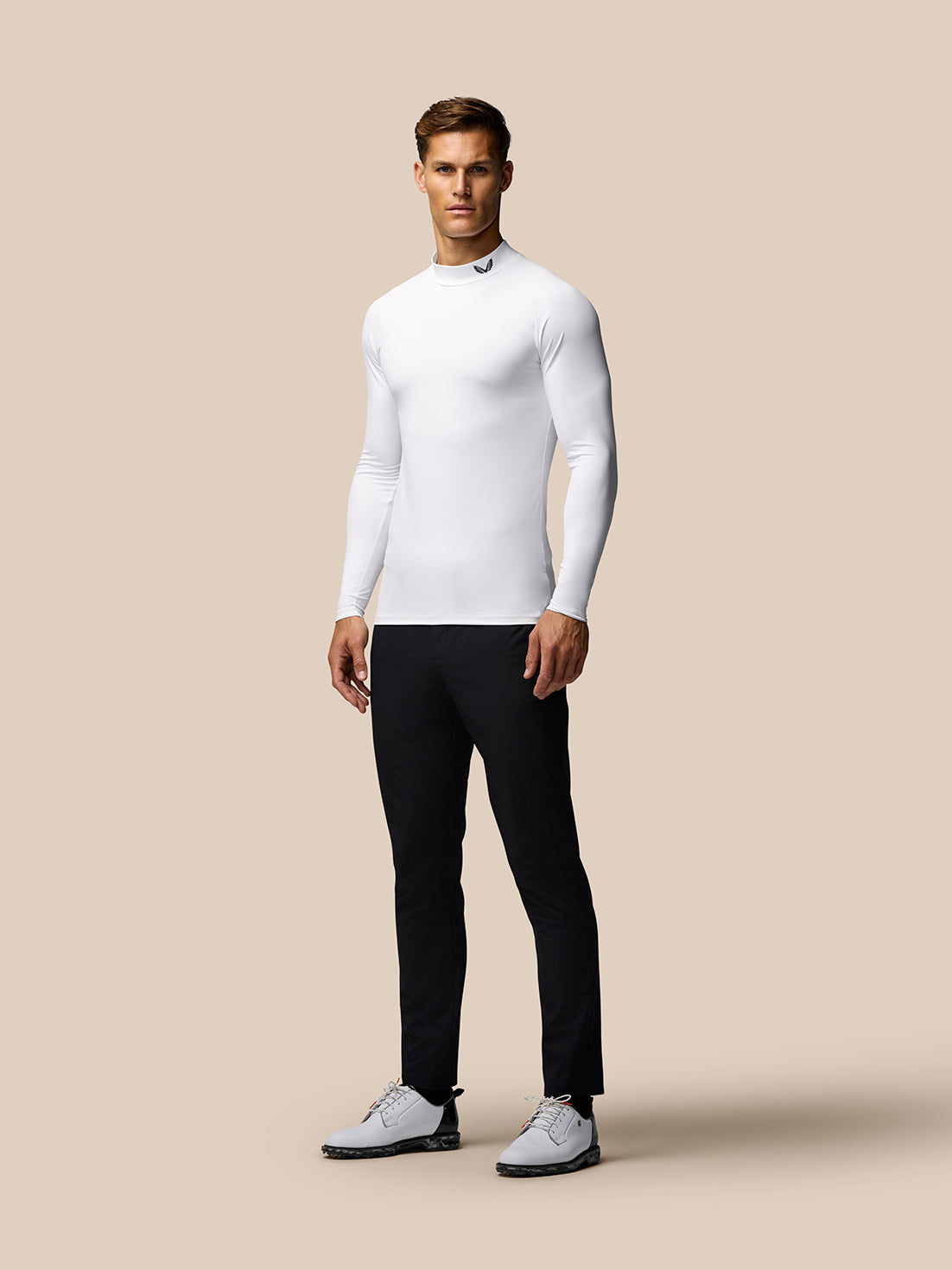 Angled front view of male model in white long sleeve golf base layer with mock neck against beige backdrop