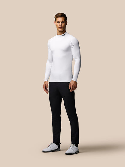 Angled front view of male model in white long sleeve golf base layer with mock neck against beige backdrop