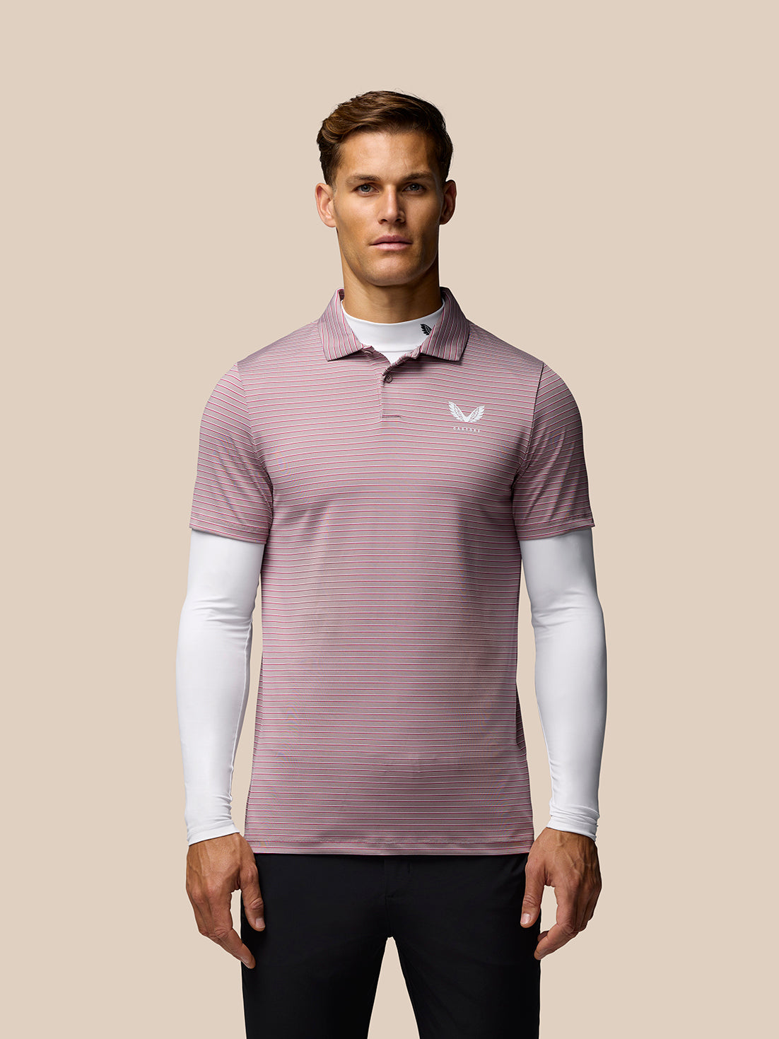 Male model in a pink striped polo over a white base layer with a small Castore emblem at the neck