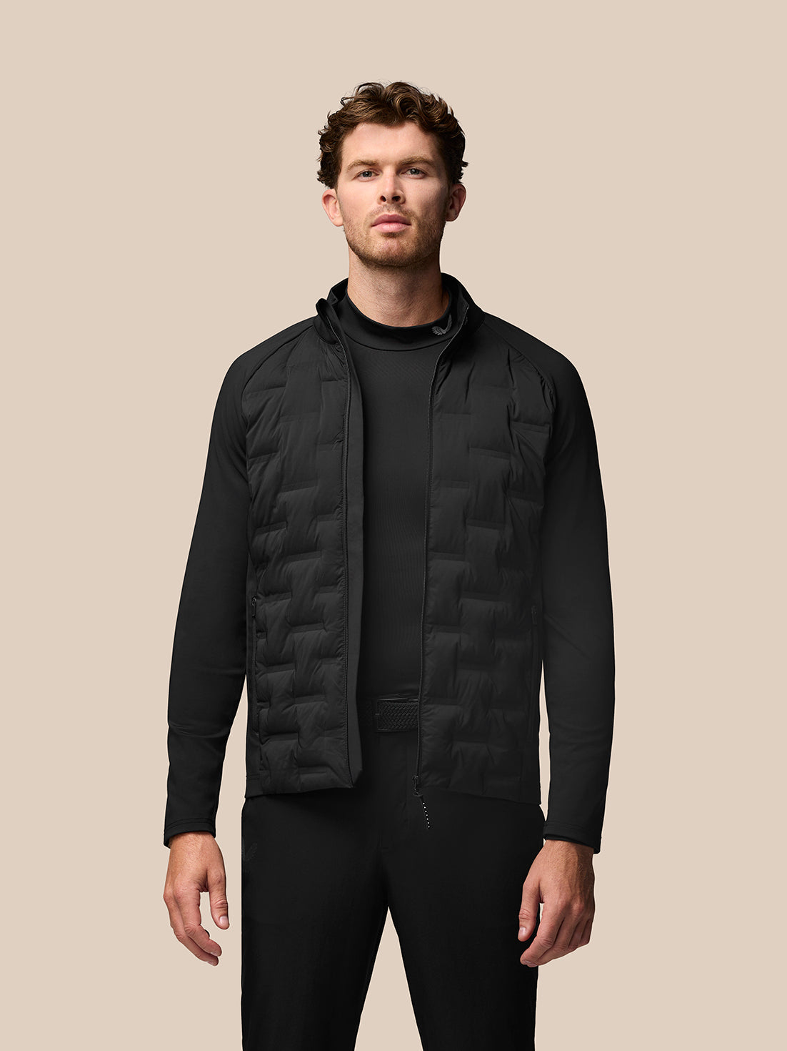 Male model in black golf layering set with a quilted vest over a base layer against a beige background