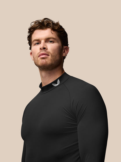 Male model wearing black golf long sleeve base layer with stand collar and Castore branding at collar and sleeve