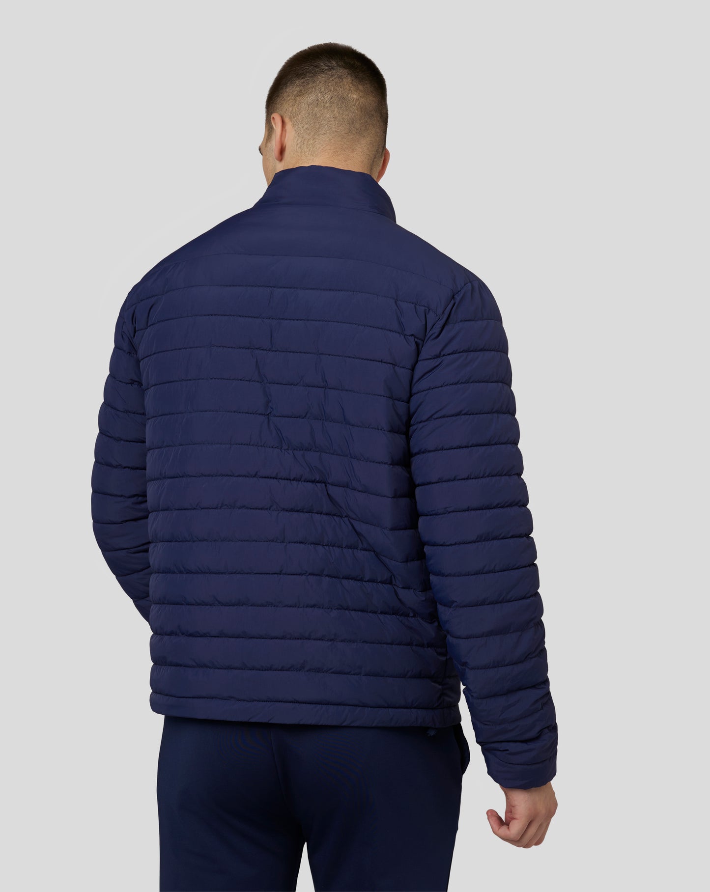 Back view of a navy Castore travel lightweight puffer jacket with horizontal quilting.