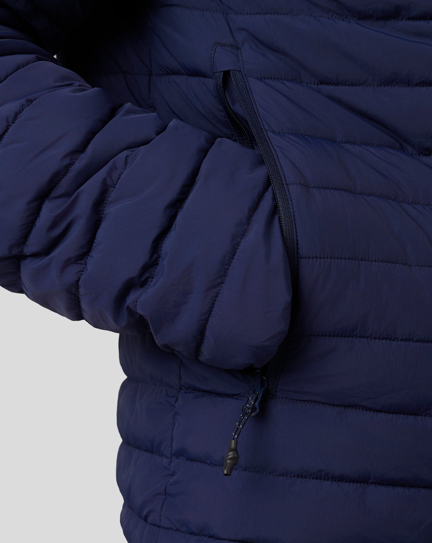 Close up of navy puffer jacket zipper along the side pocket with quilted panels.