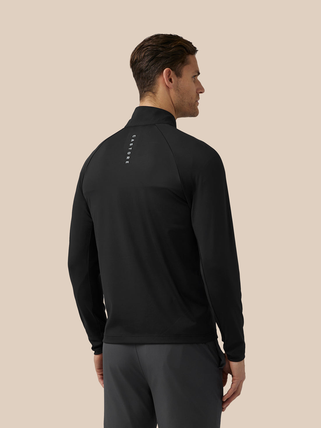 Model wearing black jacket seen from behind with vertical Castore branding along the spine.