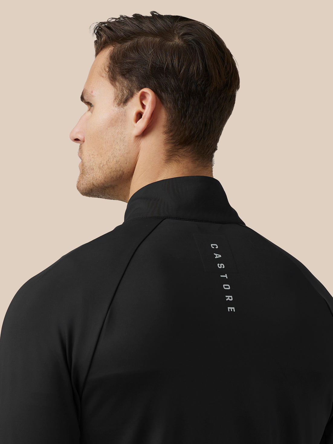 Back view of a man wearing a black golf jacket with Castore branding along the upper back.