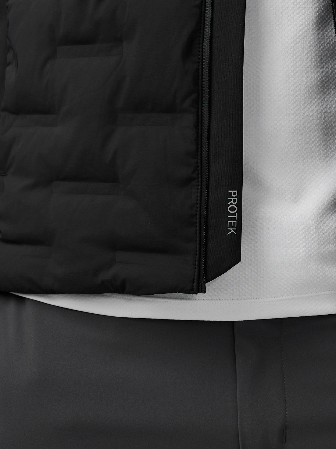 Close-up of black Protek golf jacket showing a vertical zipper and branding on the side panel.