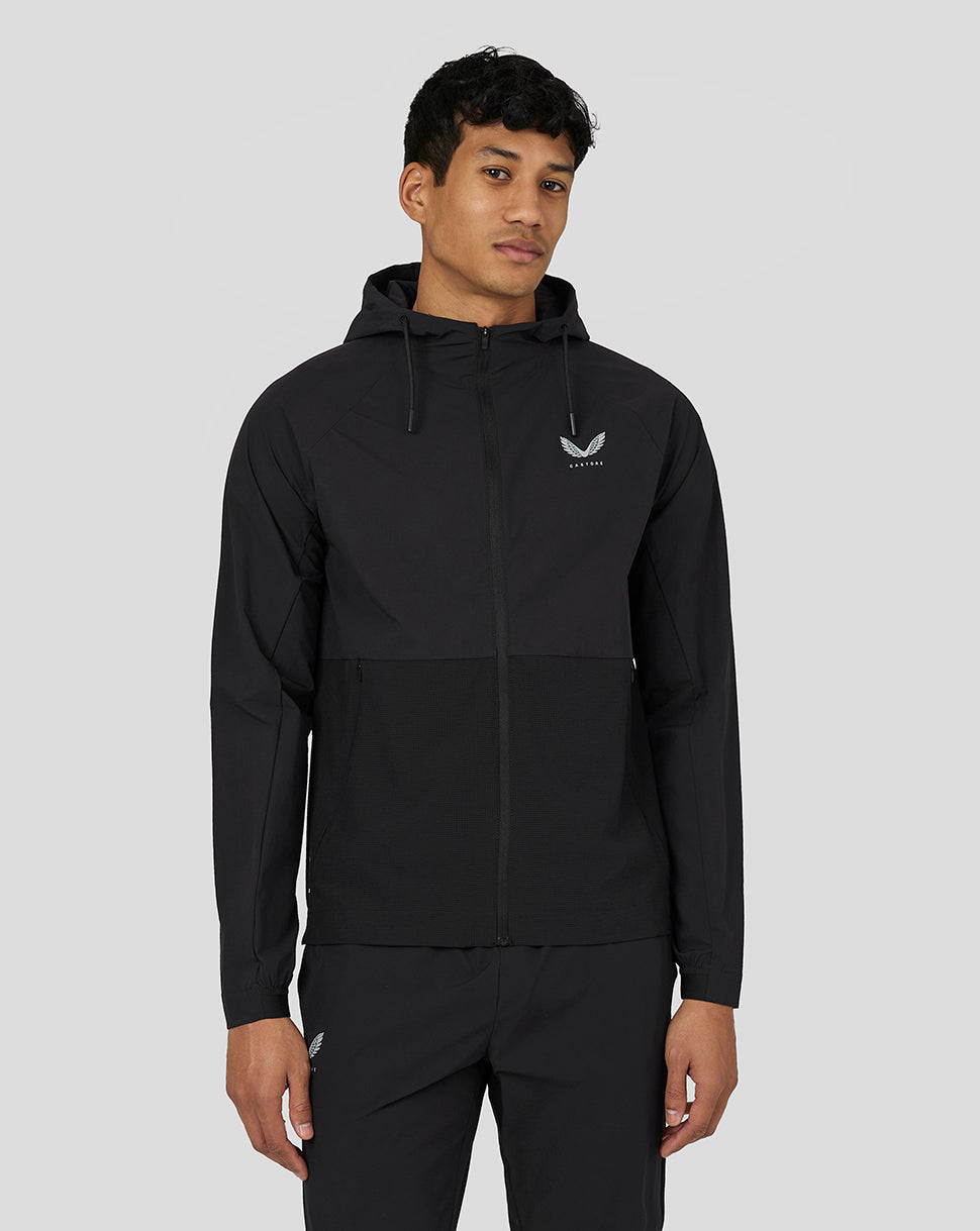 Full body shot of a man wearing a black Castore lightweight woven jacket with hood and front zipper