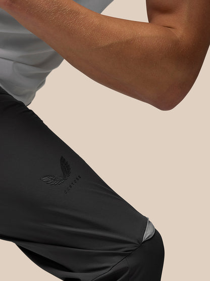 Close up of dark Flex jogger fabric with Castore branding on the right leg and left thigh against a beige background.