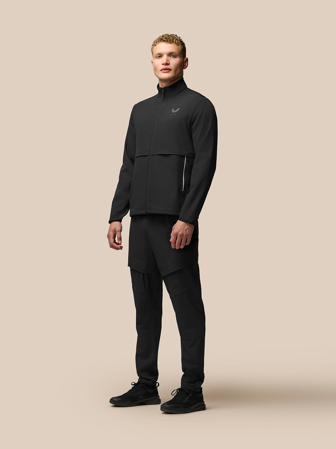 Full-body shot of a man in black Lightweight Flex Cargo Joggers and matching zip jacket, showing cargo pockets