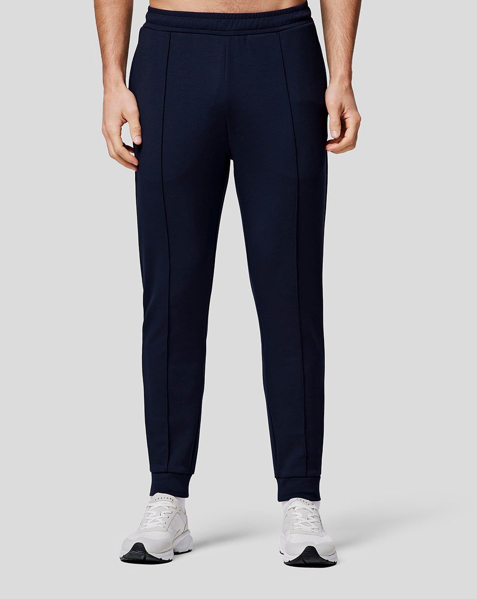 Lower half of model wearing navy recovery joggers with orange side stripe and white sneakers