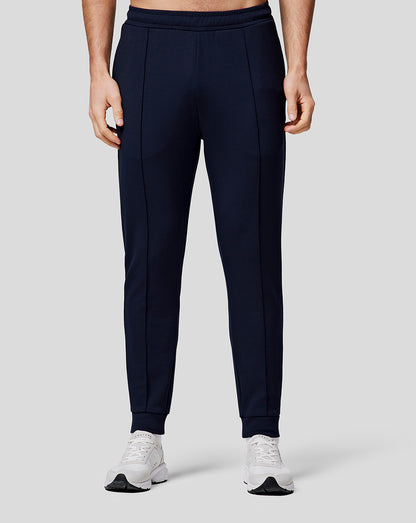 Lower half of model wearing navy recovery joggers with orange side stripe and white sneakers