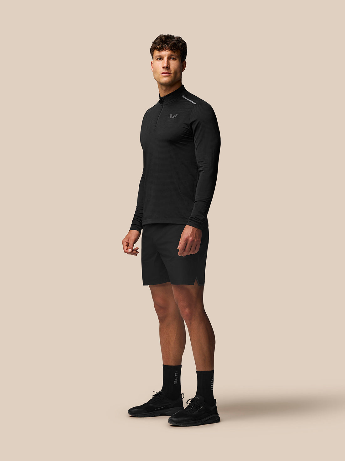 Male model wearing black Apex Training Shorts with a matching top on a beige studio backdrop