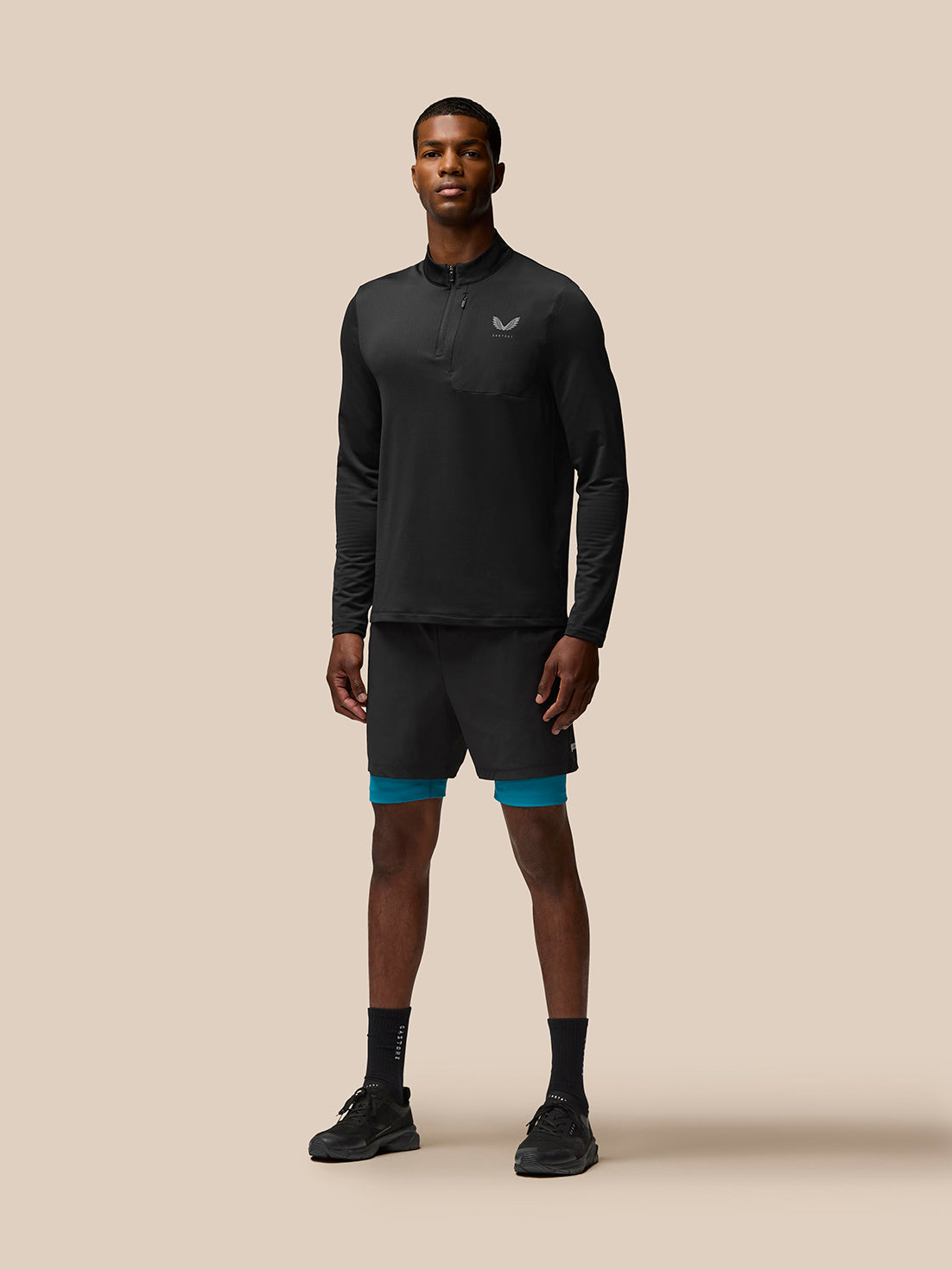 Male model wearing Flow Training Shorts in dark aqua with teal underlayer visible beneath black outer shorts