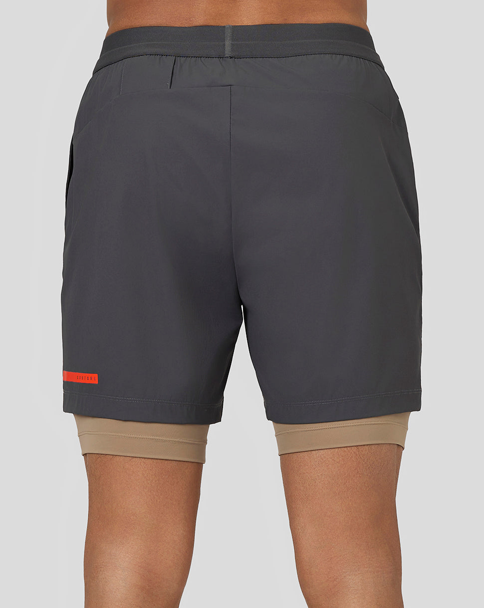 Back view of gunmetal Flow Training Shorts with drawstring waistband and orange branding on hem, beige liner peeking out.