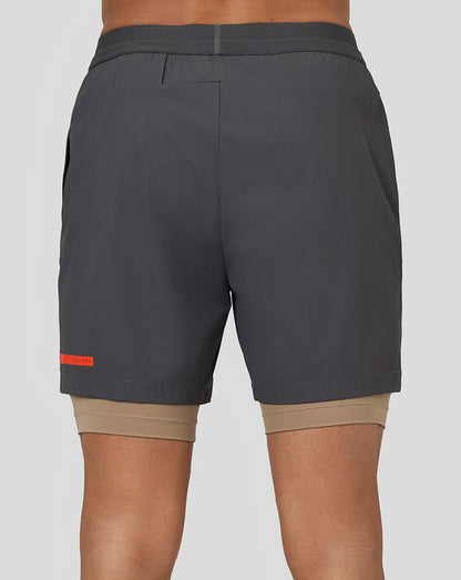 Back view of gunmetal Flow Training Shorts with drawstring waistband and orange branding on hem, beige liner peeking out.