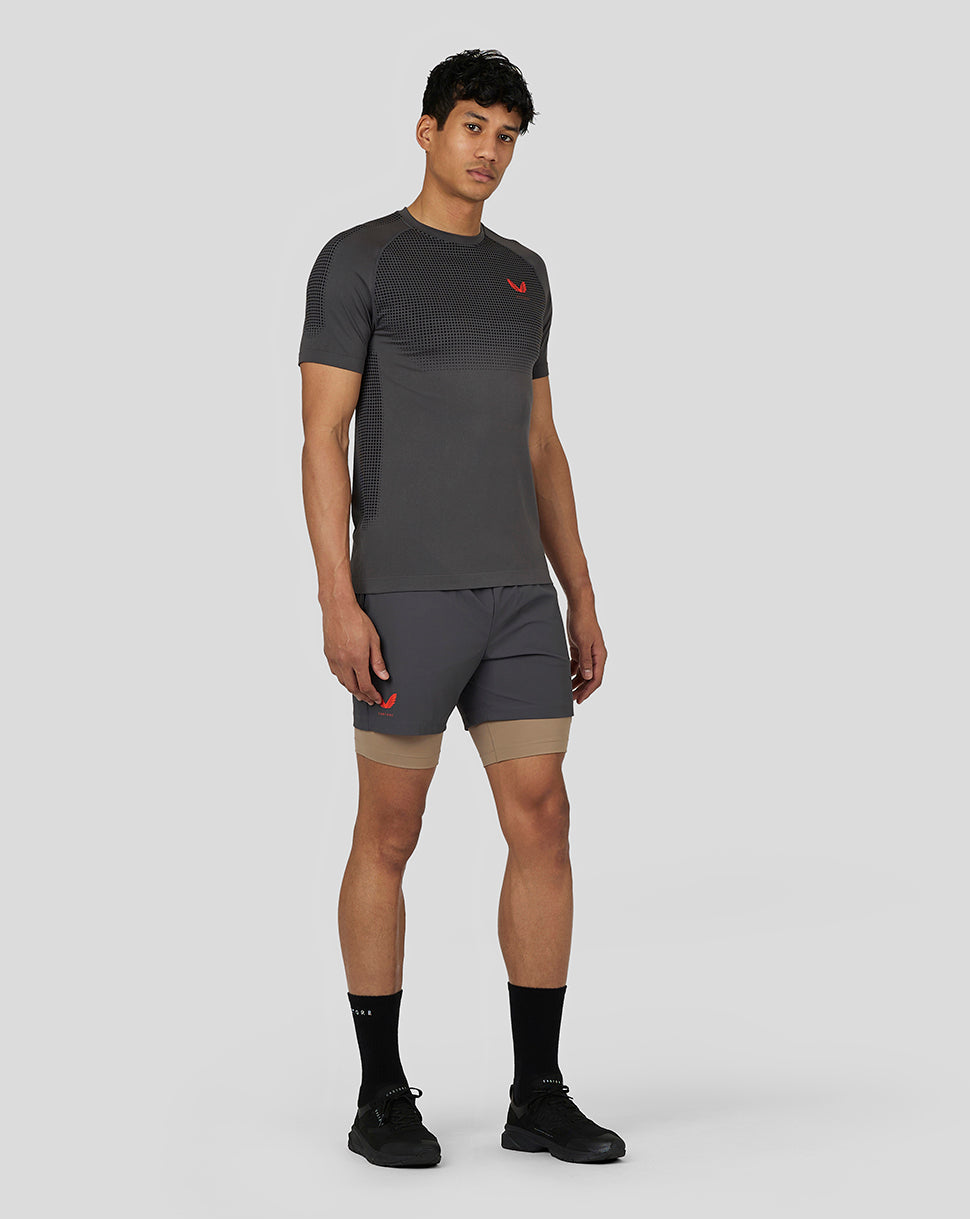 Male model wearing gunmetal Flow Training Shorts over beige liner, showcasing athletic fit and side branding.