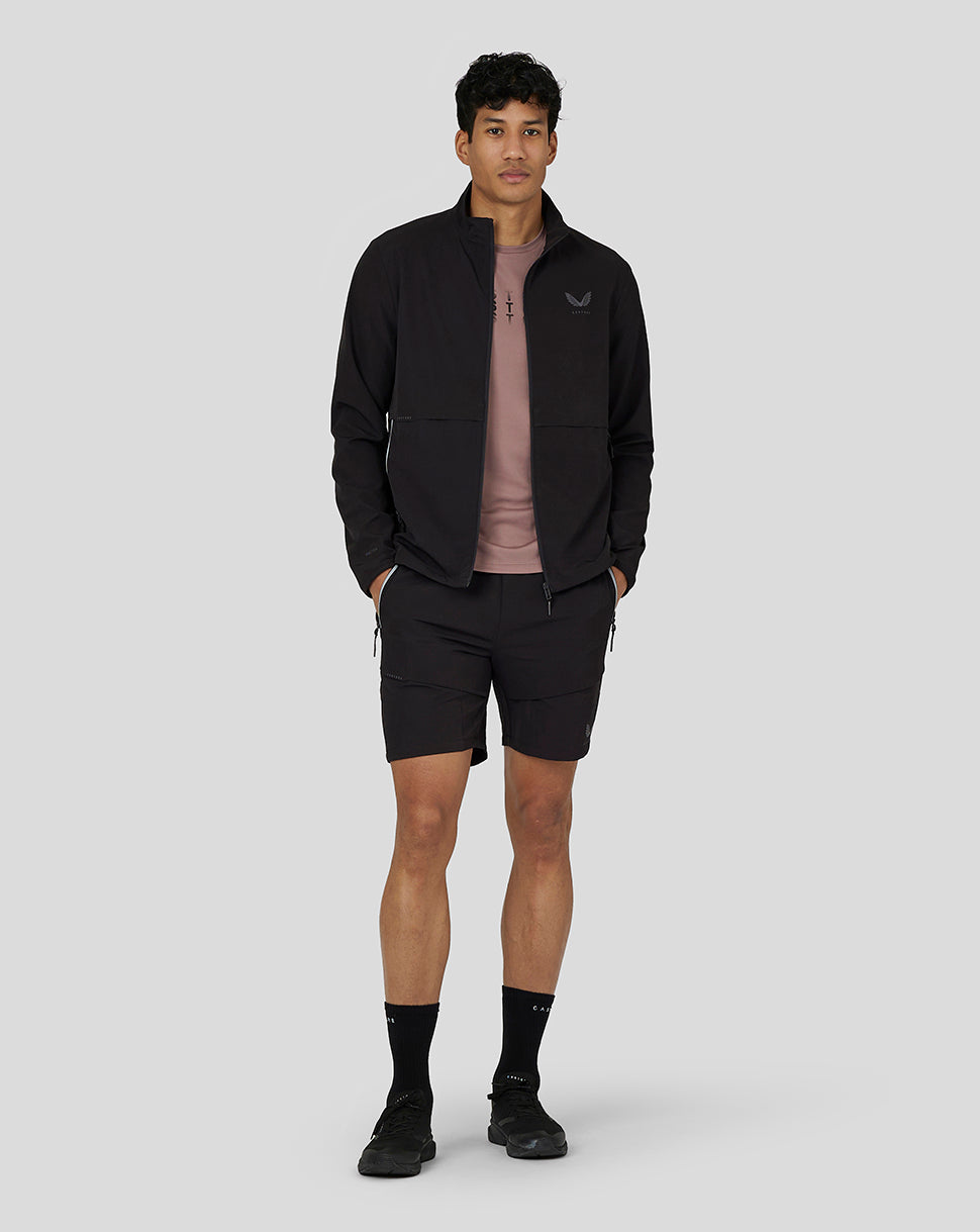 Full-body shot of a man wearing a black zip jacket, pink shirt, and black Flex Woven Cargo Shorts.