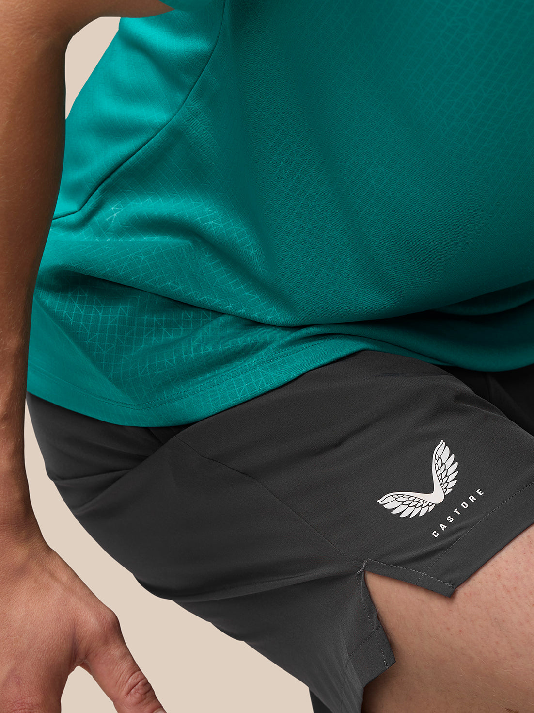 Side view of a model wearing teal top and black Adapt shorts with Castore branding on the thigh.