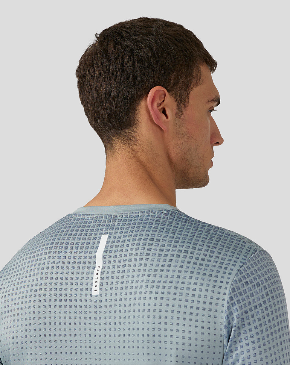 Back view of a man wearing a stone blue lightweight knit T shirt with a vertical Castore branding stripe